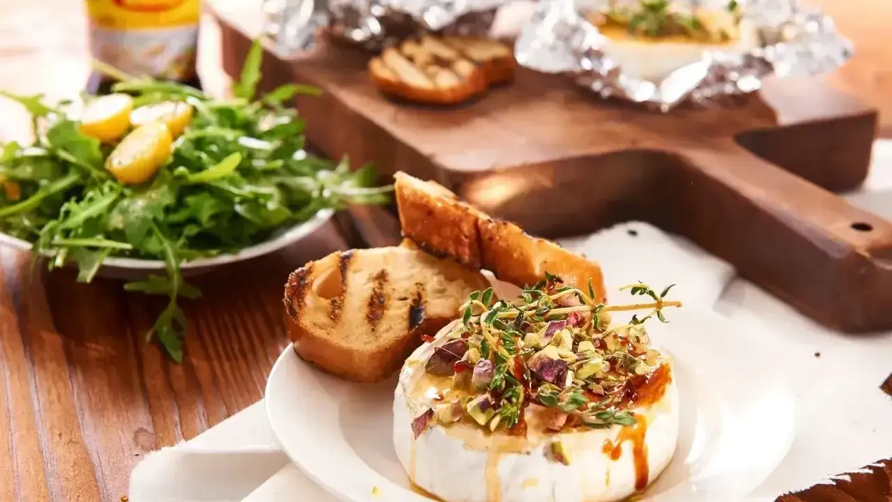 Pyszny camembert na grilla, polany miodem i posypany pistacjami, podany z grzankami i sałatką. Idealna przekąska na letnie wieczory.