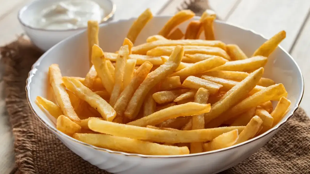 Chrupiące frytki z airfryer w białej misce, obok sos. Idealna przekąska na szybki obiad.