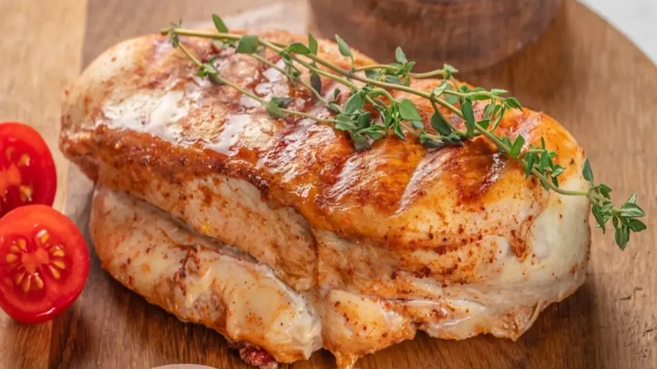 Soczysty filet z indyka, pieczony z ziołami, podany z pomidorkami koktajlowymi na drewnianej desce.