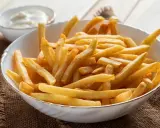 Chrupiące frytki z airfryer w białej misce, obok sos. Idealna przekąska na szybki obiad.