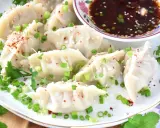 Pyszne pierogi gyoza, posypane szczypiorkiem i sezamem, podane z sosem.