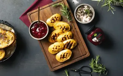Grillowane oscypki z żurawiną, podane na desce z gałązką rozmarynu, obok miseczki z konfiturą i słoiczka z żurawiną.