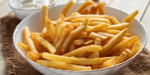 Chrupiące frytki z airfryer w białej misce, obok sos. Idealna przekąska na szybki obiad.