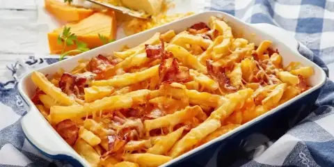 Zapiekane frytki z serem i chrupiącym boczkiem, podane w niebieskiej brytfance na kratkowanym obrusie.