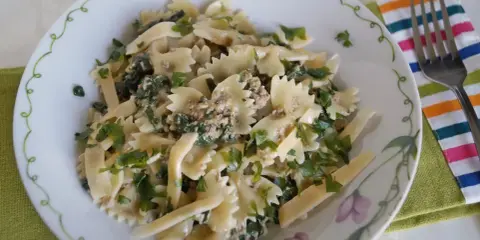 Pyszny makaron farfalle z tuńczykiem i szpinakiem, posypany świeżą natką pietruszki. Idealny na szybki obiad.