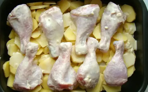 Osiem pałek kurczaka w sosie, ułożonych na plastrach ziemniaków w brytfannie. Idealne do pieczenia, by uzyskać chrupiące pałki z kurczaka w piekarniku.