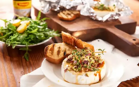 Pyszny camembert na grilla, polany miodem i posypany pistacjami, podany z grzankami i sałatką. Idealna przekąska na letnie wieczory.