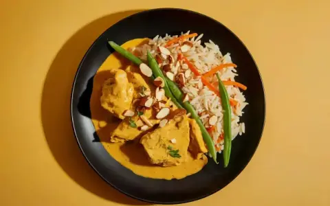 Aksamitny kurczak curry w kremowym sosie, podany z ryżem basmati, fasolką szparagową i płatkami migdałów.