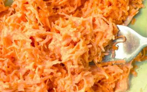 Pyszna surówka z marchewki jak z restauracji, kremowa i apetyczna. Widok z bliska na starte marchewki z sosem.