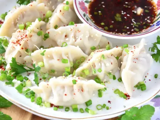 Pyszne pierogi gyoza, posypane szczypiorkiem i sezamem, podane z sosem.