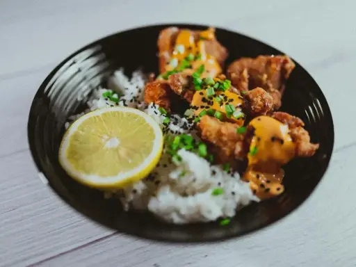 Chrupiące karaage z ryżem, posypane sezamem i szczypiorkiem, podane z plasterkiem cytryny.