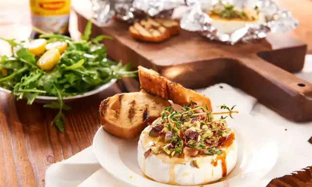 Pyszny camembert na grilla, polany miodem i posypany pistacjami, podany z grzankami i sałatką. Idealna przekąska na letnie wieczory.