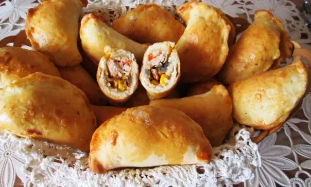Złociste pierogi meksykańskie z kurczakiem, kukurydzą i papryką, ułożone w koszyku na białej serwetce.