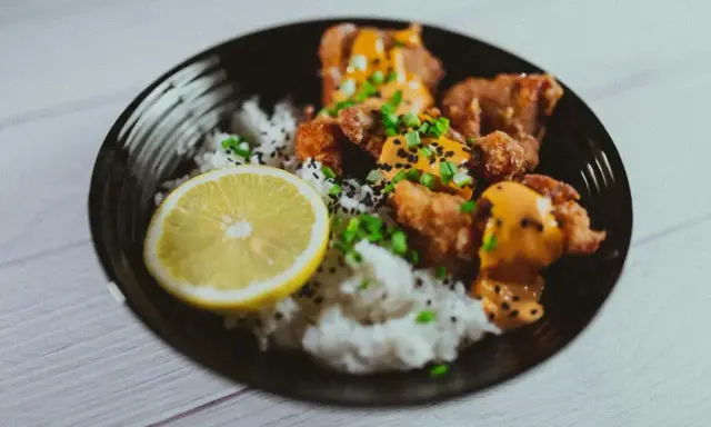 Chrupiące karaage z ryżem, posypane sezamem i szczypiorkiem, podane z plasterkiem cytryny.