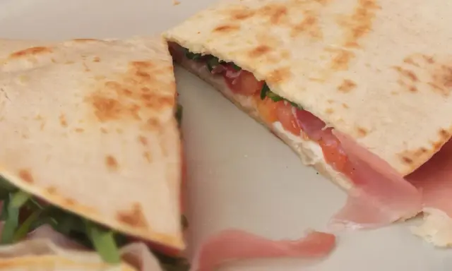 Pyszna piadina z szynką, pomidorami i rukolą, złożona na pół, prezentuje apetyczny przekrój.