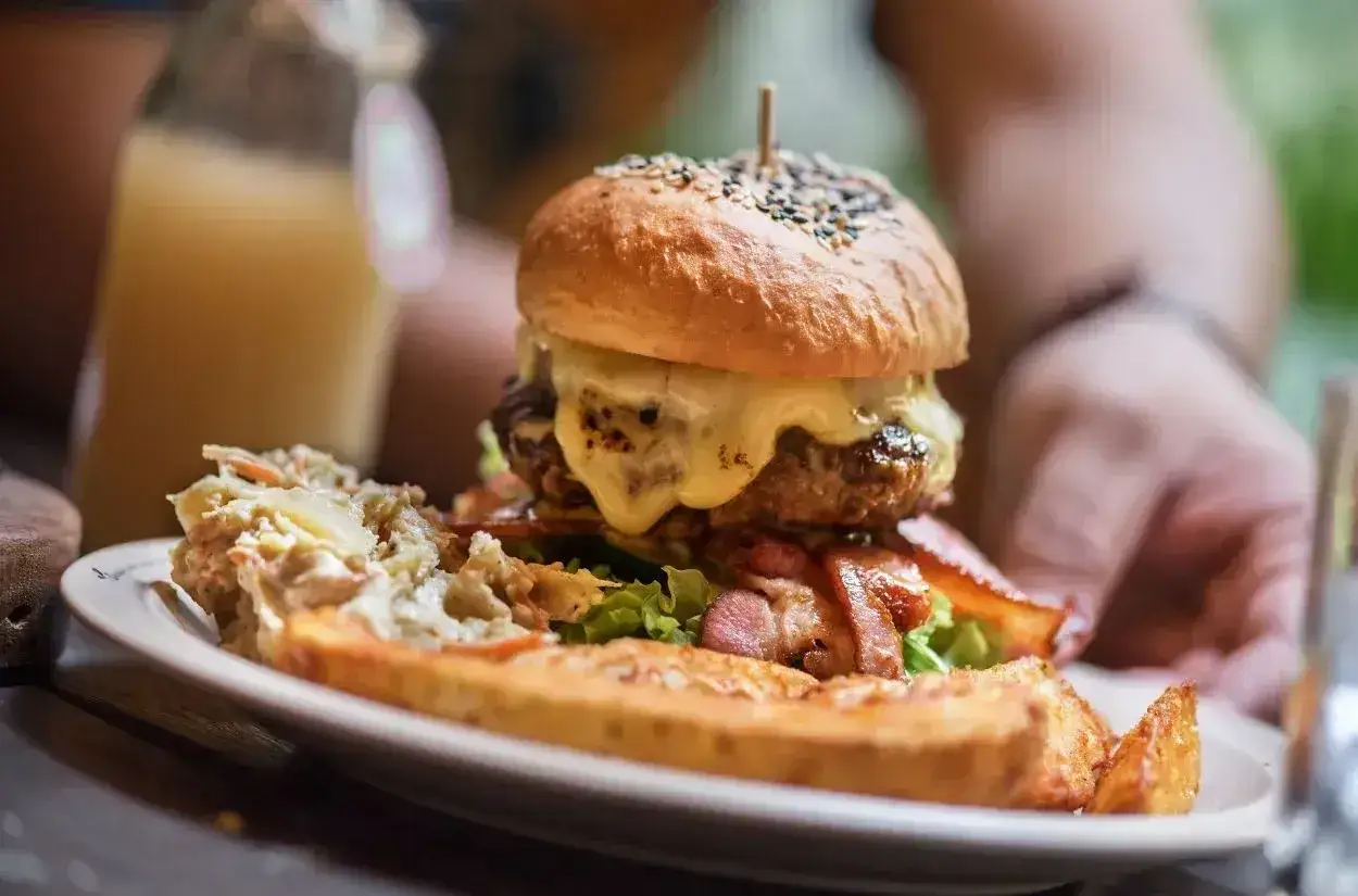 Apetyczny burger drwala z rozpływającym się serem, chrupiącym boczkiem i surówką na talerzu.