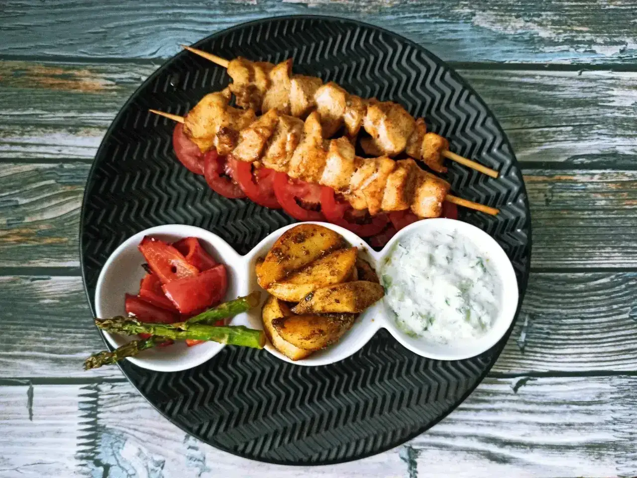 Dwa szaszłyki z kurczaka, czyli pyszne souvlaki, podane z pieczonymi ziemniakami, papryką i sosem tzatziki.