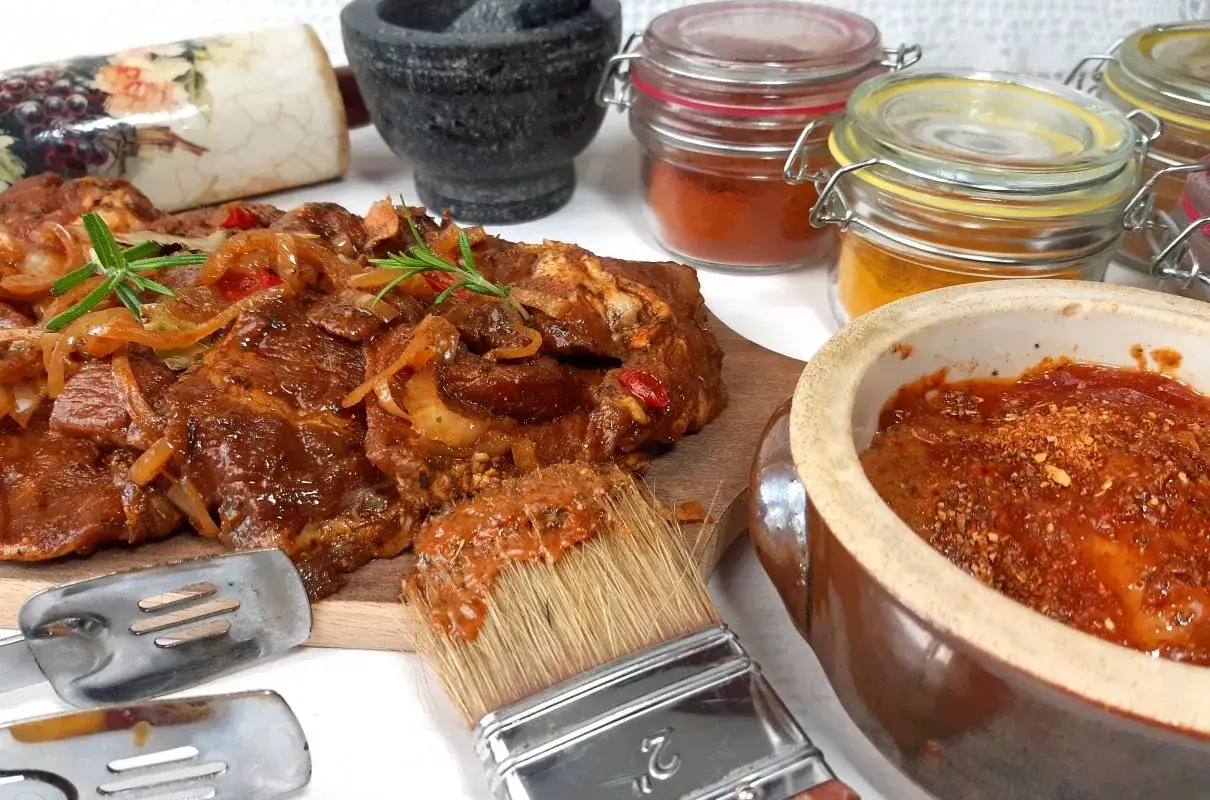 Karkówka na grilla w aromatycznej marynacie, gotowa do okrasy. Obok pędzel z sosem i przyprawy.