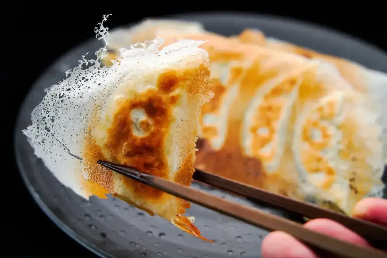 Chrupiące pierogi gyoza, złociste i apetyczne, podniesione pałeczkami.