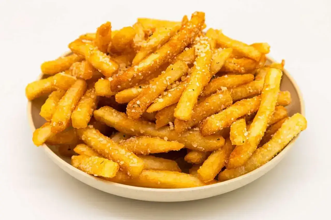 Złociste, chrupiące frytki z airfryer, posypane parmezanem i ziołami, kuszą apetycznym wyglądem.
