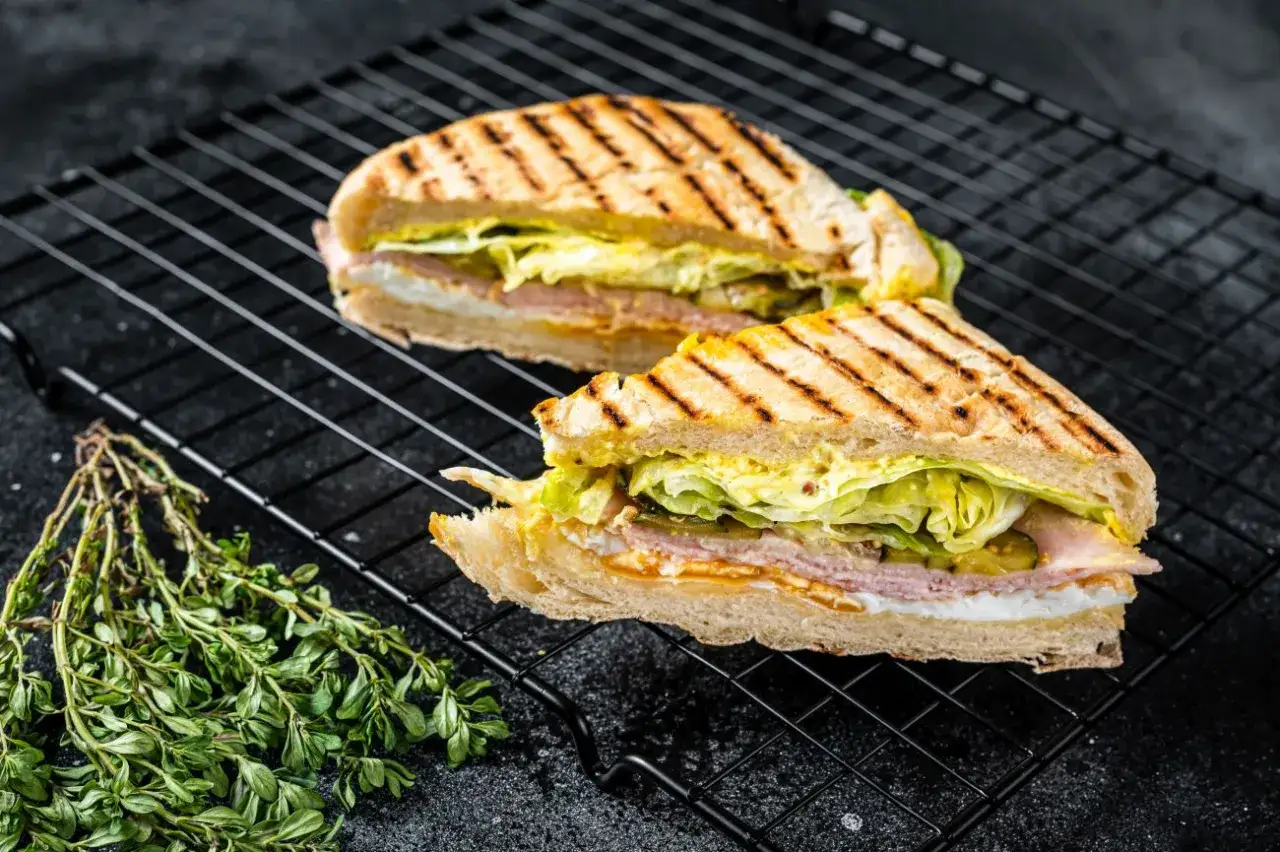 Dwa pyszne, grillowane panini z szynką, serem, sałatą i ogórkiem konserwowym na czarnej kratce.