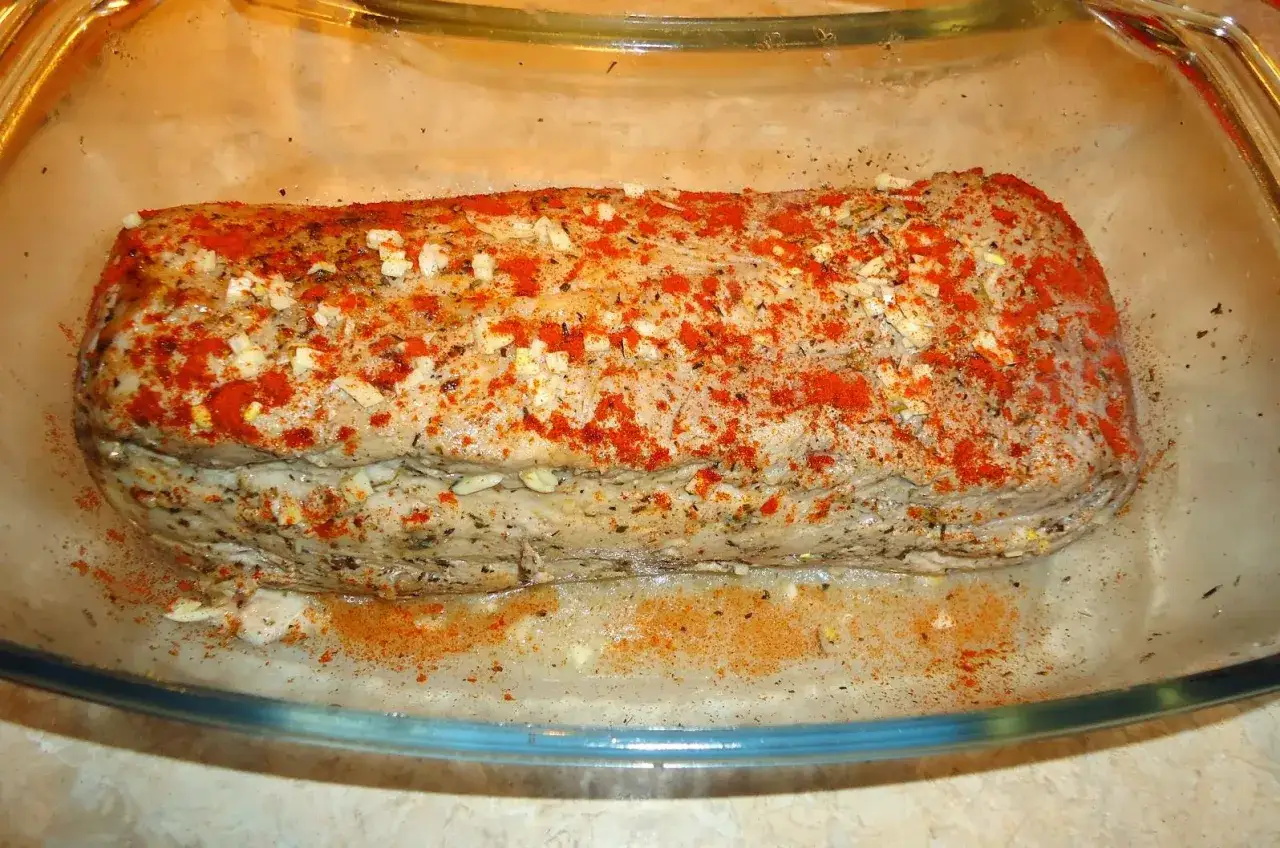 Gotowy do pieczenia schab, obficie przyprawiony papryką, czosnkiem i ziołami, leży w szklanej formie.