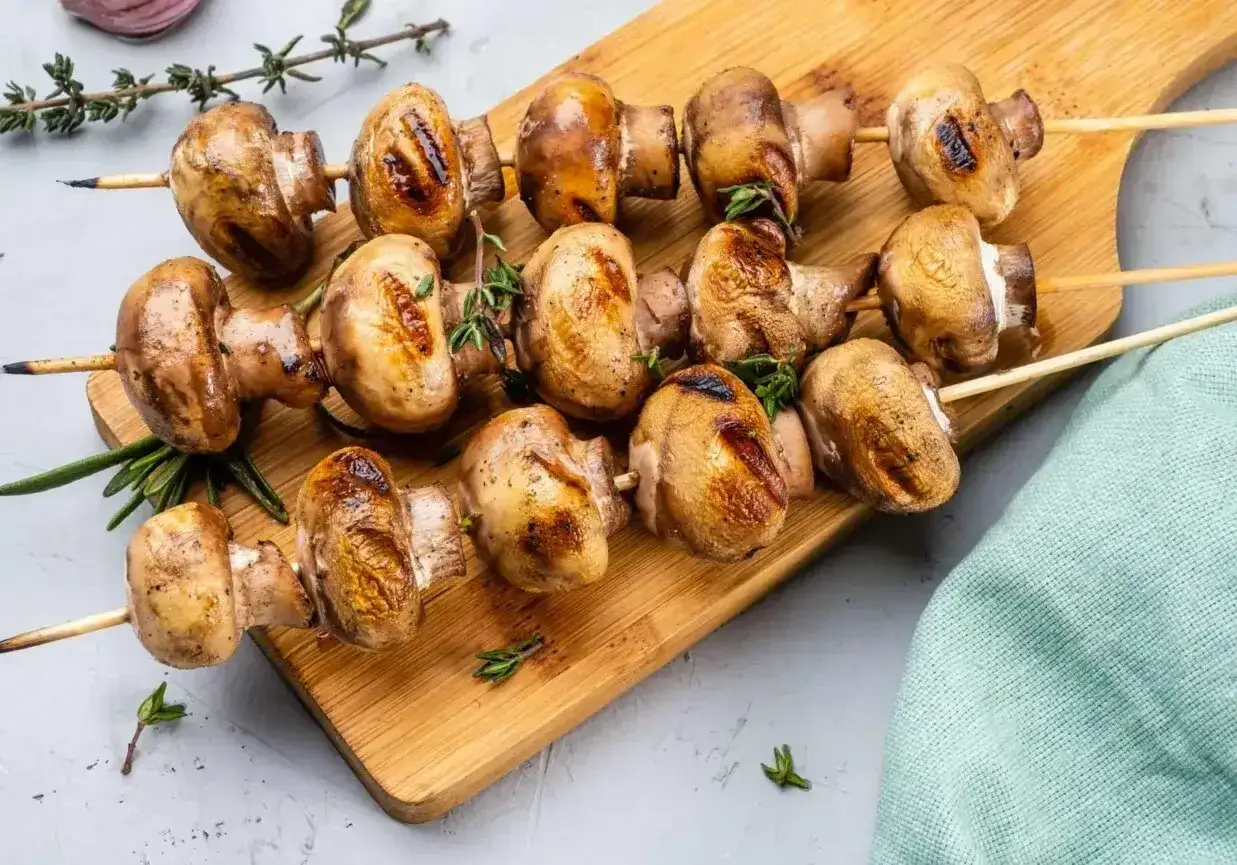 Aromatyczne pieczarki z grilla na drewnianej desce, ozdobione ziołami. Idealna przekąska na letnie wieczory.