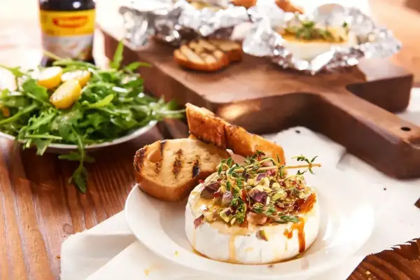 Pyszny camembert na grilla, polany miodem i posypany pistacjami, podany z grzankami i sałatką. Idealna przekąska na letnie wieczory.